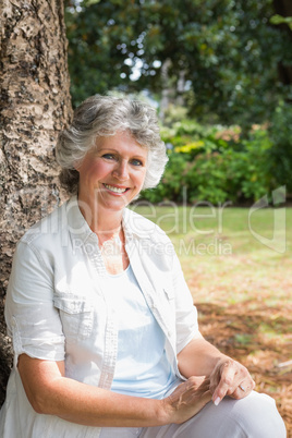 Cheerful mature woman sitting on tree trunk