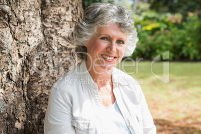 Happy mature woman sitting on tree trunk