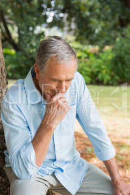 Thoughtful retired man sitting on tree trunk with head bowed