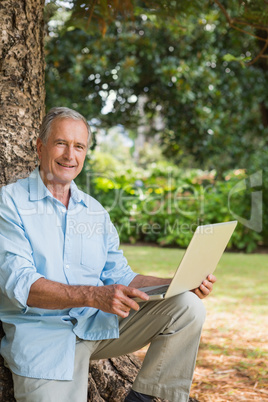 Old man leaning against tree with a laptop