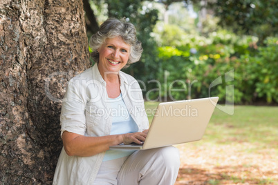 Mature woman using a laptop sitting on tree trunk Mature woman using a laptop sitting on tree trunk
