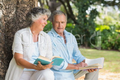 Older couple reading books together sitting on tree trunk