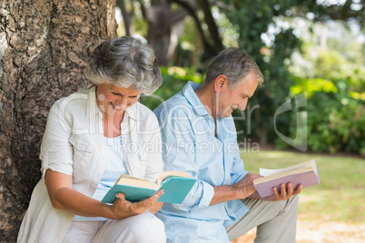 Retired couple reading books together sitting on tree trunk