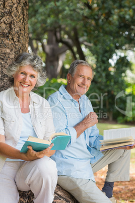 Happy older couple reading books together sitting on tree trunk