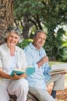 Happy older couple reading books together sitting on tree trunk