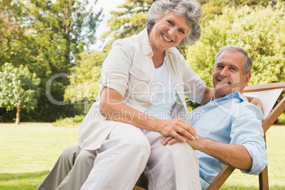 Happy mature woman sitting on her husband on deck chair