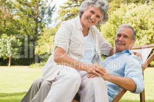 Happy mature woman sitting on her husband on deck chair