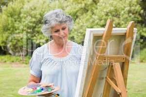 Content mature woman painting on canvas