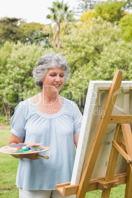 Cheerful mature woman painting on canvas