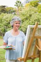 Cheerful mature woman painting on canvas