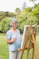 Cheerful retired woman painting on canvas