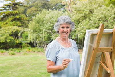 Smiling retired woman painting on canvas