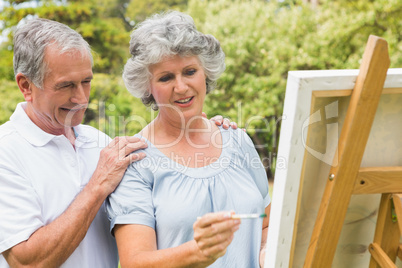 Happy retired woman painting on canvas and talking with husband