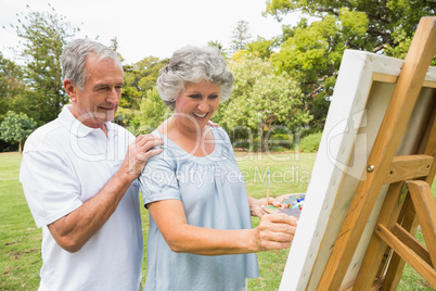 Content retired woman painting on canvas and talking with husban