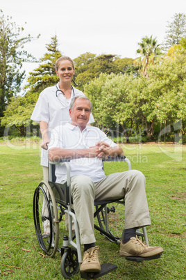Happy man sitting in a wheelchair with his nurse pushing him