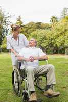 Happy man sitting in a wheelchair talking with his nurse pushing
