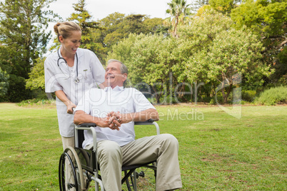 Smiling man sitting in a wheelchair talking with his nurse pushi