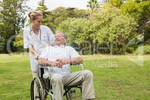 Smiling man sitting in a wheelchair talking with his nurse pushi