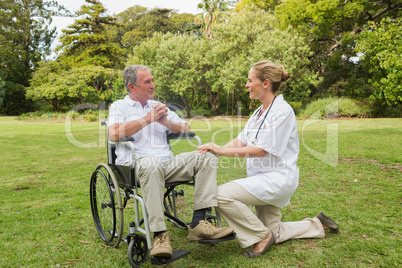 Smiling man in a wheelchair talking with his nurse kneeling besi