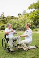 Happy man in a wheelchair talking with his nurse kneeling beside