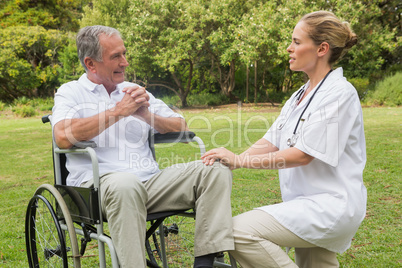 Cheerful man in a wheelchair talking with his nurse kneeling bes