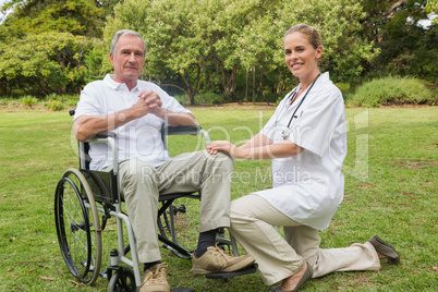 Cheerful man in a wheelchair with his nurse kneeling beside