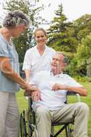 Happy man in a wheelchair talking with his nurse and wife