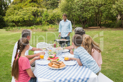 Cheerful extended family watching father at the barbecue