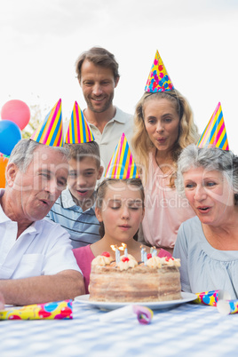 Cheeful family watching girl blowing out candles at birthday par
