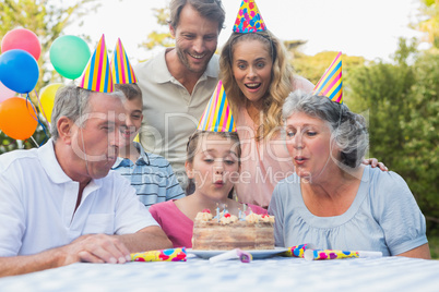 Cheerful extended family watching girl blowing out birthday cand