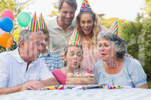 Cheerful extended family watching girl blowing out birthday cand