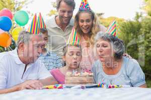 Happy extended family watching girl blowing out birthday candles