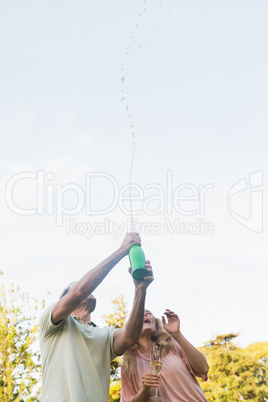 Handsome man spraying bottle of champagne with blonde partner