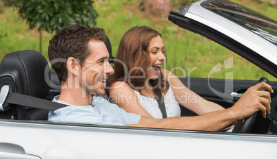 Laughing couple driving in a silver convertible