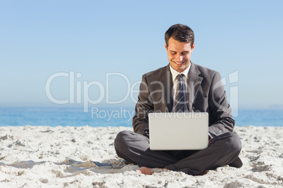 Young businessman with legs crossed typing on his laptop