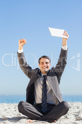 Victorious young businessman holding up his tablet computer