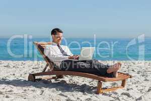 Young businessman lying on a deck chair with his laptop