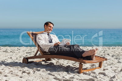 Young businessman relaxing on a deck chair using his tablet