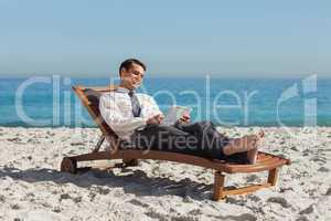 Young businessman relaxing on a deck chair using his tablet