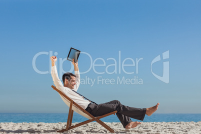 Victorious young businessman resting on his deck chair holding h