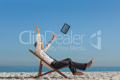 Victorious young businessman on his deck chair throwing his tabl