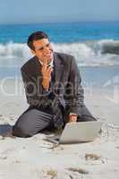 Smiling businessman sitting on the sand with his laptop