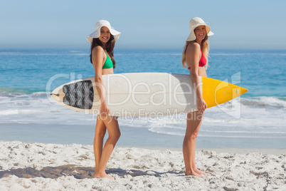 Two women in bikinis holding a surfboard