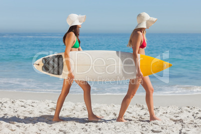 Two attractive women in bikinis holding a surfboard