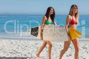 Two gorgeous women in bikinis holding a surfboard