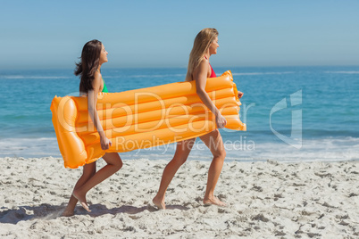 Two pretty friends running holding air mattress