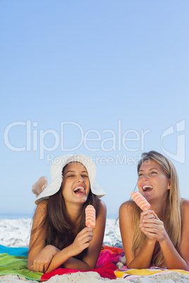 Smiling pretty women lying on their towel eating ice cream