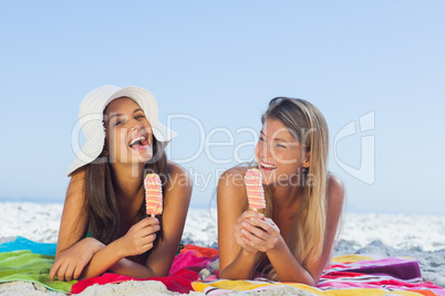 Cheerful pretty women lying on their towel eating ice cream