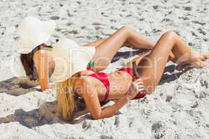 Attractive women in bikinis lying on the sand drinking beer