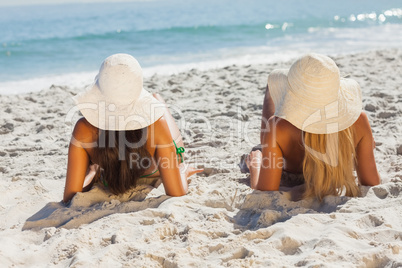 Attractive blonde and brunette in bikinis lying on the sand